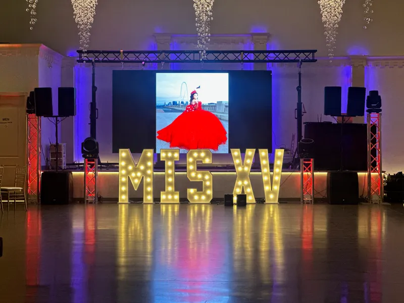 Light-up MIS XV marquee letters in front of an LED video wall showing a quinceañera in a red gown at the Dallas Reunion Tower, set up by DJ Oso